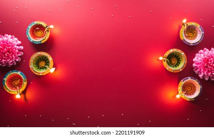 Happy Diwali - Clay Diya lamps lit during Diwali, Hindu festival of lights celebration. Colorful traditional oil lamp diya on red background - Shutterstock ID 2201191909