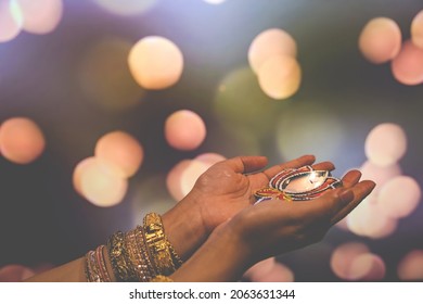 Happy Diwali - Woman hands with henna holding lit candle isolated on dark background. Clay Diya lamps lit during Dipavali, Hindu festival of lights celebration. Copy space for text. - Shutterstock ID 2063631344