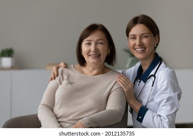 Happy Doctor And Grateful Senior Patient Smiling At Camera At Appointment. Physician Giving Geriatric Care, Medical Help, Support To Older Woman, Touching Shoulders, Hugging. Head Shot Portrait