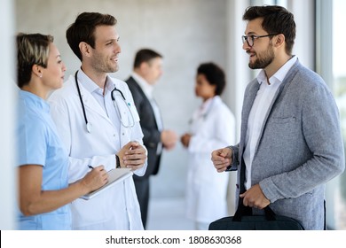 Happy doctor and nurse communicating with a businessman while standing in a hallway at medical clinic. 