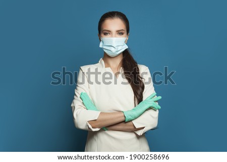 Happy doctor or nurse woman in protective medical mask and surgical gloves on blue background.  Medicine, assistance, safety and virus covid-19 protection concept