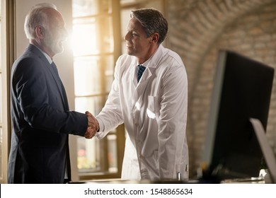 Happy doctor and senior businessman greeting each other while shaking hands at clinic.  - Shutterstock ID 1548865634