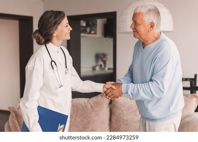 Happy doctor and senior man patient smiling and shaking hands before medical interview at home. Mature grandpa getting acquainted with friendly young nurse or physician. Health, care and trust concept - Powered by Shutterstock