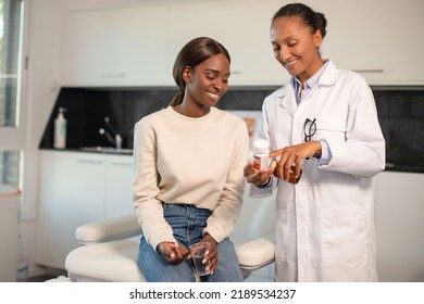 Happy doctor showing vitamins to smiling female patient. Young African American woman sitting at doctors office holding cup of water. Prescription medicine concept - Powered by Shutterstock