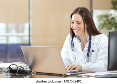 Happy doctor using a laptop writing content at consultation