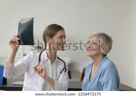 Happy doctor woman showing Xray scan to elder patient, explaining shot of bones, radiography screening film to senior woman in hospital office. Old lady visiting doctor for medical checkup