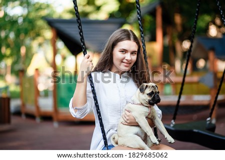 Happy dog ​​and girl. The girl is playing with a dog. Young woman walking with a pug dog in summer park. Portrait of a pug. Portrait of a beautiful pug puppy. The dog is lying on the ground.