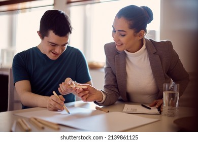 Happy down syndrome man and his psychologist drawing together on the paper during home visit. - Shutterstock ID 2139861125