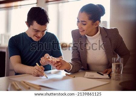 Happy down syndrome man and his psychologist drawing together on the paper during home visit.