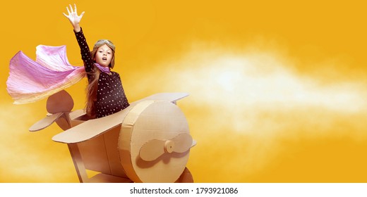 Happy Dreamer Girl Playing With A Cardboard Airplane. Childhood. Fantasy, Imagination. Studio Portrait On A Yellow Background.