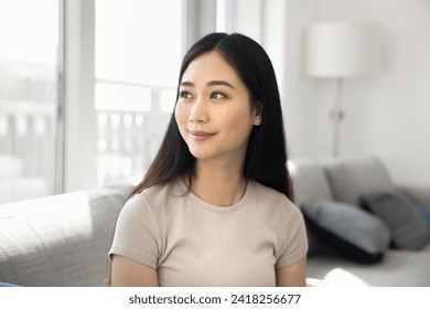 Happy dreamy beautiful Chinese girl sitting on sofa at home, looking at window away with dreamy thoughtful face, smiling. Positive young 20s Asian woman casual portrait - Powered by Shutterstock