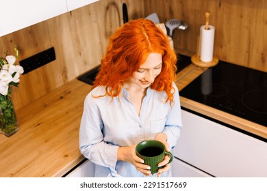 Happy dreamy senior blonde lady enjoying good morning, drinking hot coffee at home, resting on comfortable couch in cozy living room, holding ceramic mug, cup of tea, smiling, looking away - Powered by Shutterstock