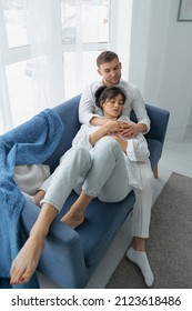 Happy dreamy young caucasian couple rest cuddle on couch in room thinking or visualizing, smiling millennial man and woman relax on sofa at home, hug and embrace.