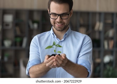 Happy dreamy young handsome ceo executive manager in eyewear holding in hands small green plant, symbol of developing new successful project, eco-friendly sustainable company growth path concept. - Shutterstock ID 2067222929