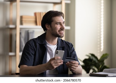 Happy dreamy young man entering payment information from credit bank card in mobile shopping application, buying goods or services online, satisfied with fast financial operation, cyber security.