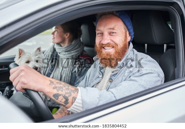 Happy\
to drive new car. Handsome young man in smart casual wear smiling\
while driving a car with his girlfriend and a\
dog