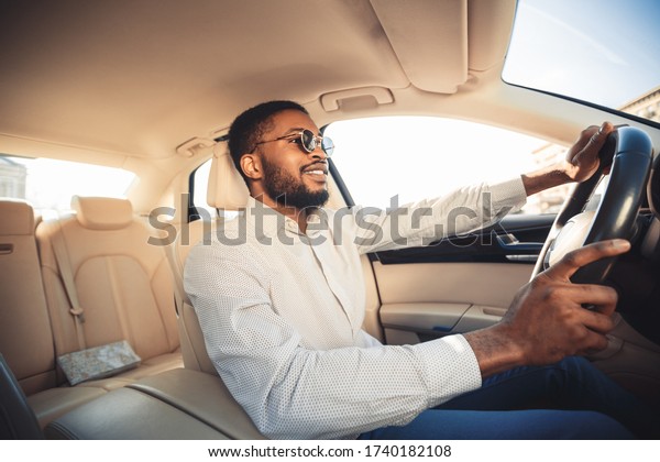 Happy Driver. African Man\
Driving Own New Car Sitting In Seat And Smiling. Selective\
Focus