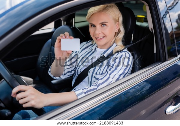 Happy driver holding license and looking at camera\
in auto