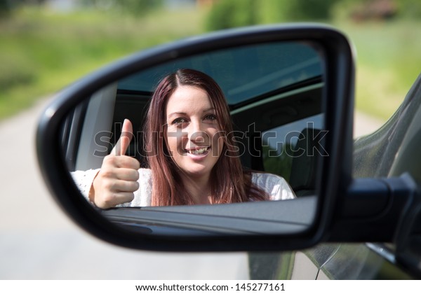 A happy driver leaning out of the window and\
showing thumbs up in the\
mirror