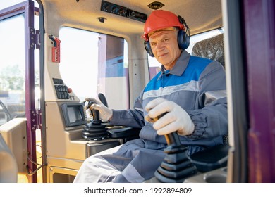 Happy Driver Man Of Industrial Dump Truck Sits In Cab And Works On Construction Building Site.