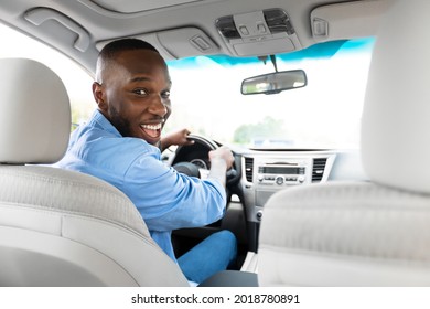 Happy Driver. Portrait Of Cheerful Positive African American Man Looking Back At Camera Sitting In A Car, View From Rear Seat. Excited Black Guy Riding In The City, Holding Hands On Steering Wheel