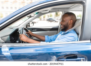 Happy Driver. Side view profile portrait of cheerful positive African American man sitting in a car on driver's seat. Excited black guy riding in the city, holding hands on steering wheel