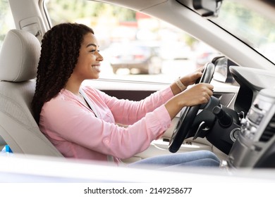 Happy Driver. Side View Profile Portrait Of Cheerful Positive African American Woman Sitting In A Car On Driver's Seat. Excited Black Lady Riding In The City, Holding Hands On Steering Wheel