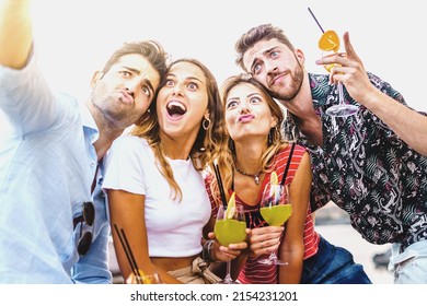 Happy drunk friends taking a selfie making faces holding alcoholic cocktails sitting on a bench outdoors in the summer - friendship love in happy hour and alcohol life style concept - Powered by Shutterstock