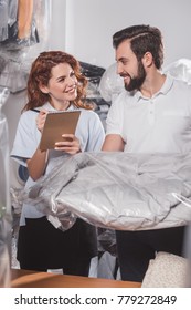 Happy Dry Cleaning Workers With Jacket In Bag At Warehouse