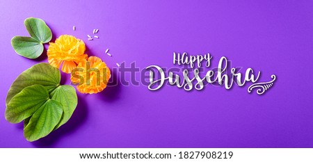 Happy Dussehra. Yellow flowers, green leaf and rice on purple pastel background. Dussehra Indian Festival concept.