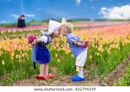 Happy Dutch children playing in blooming tulip flowers field.  Boy and girl wearing traditional national costume, wooden clogs and hat play with tulips next to a windmill in Holland, Netherlands 