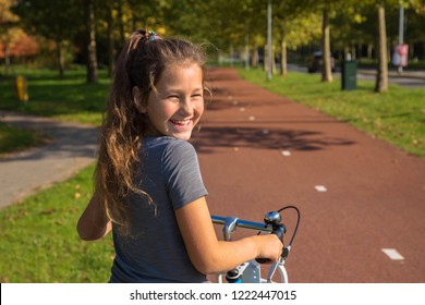 Happy dutch kid laughs. Beautiful little girl rides bike on bike path. Cyclist child or teenager girl enjoys good weather and cycling. Environmentally friendly transport concept. The Netherlands.