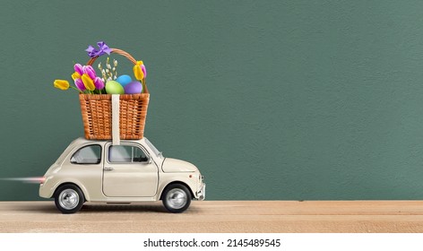 Happy Easter Background Or Card. Toy White Car Carrying Basket With Easter Eggs And Spring Flowers Atop On A Green Background. Easter Concept. Free Space