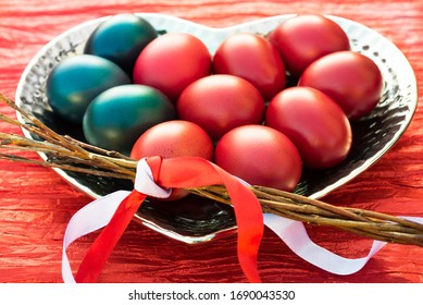 Happy Easter background. Dark red and blue Easter colored eggs on heart shaped metallic dish and wicker whip with ribbons for rejuvenating Czech girls and women at spring to stay young and healthy. 