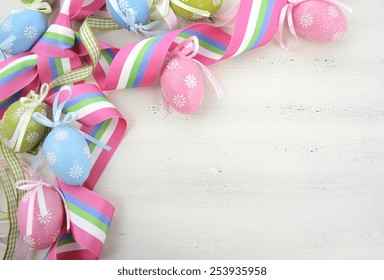 Happy Easter Background With Pink, Blue And Green Ornament Eggs And Ribbon On Vintage Style Rustic Distressed White Shabby Chic Wood Table, With Copy Space For Your Text Here.