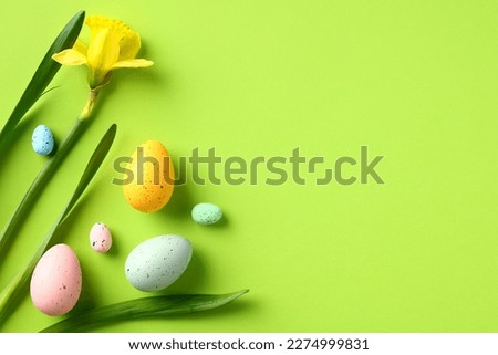 Happy Easter banner design. Daffodil flowers and colorful Easter eggs on green background. Flat lay, top view.