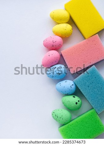 Happy Easter and cleaning concept. Easter eggs and colorful sponges on white background with copy space. Easter greating card. Top view, flat lay. Cleaning stuff and colorful eggs. Housekeeping.