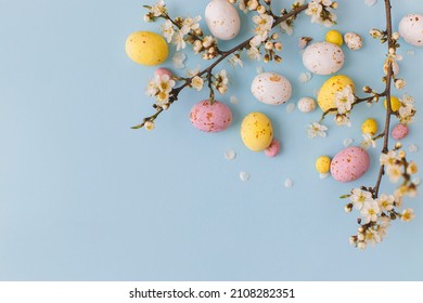 Happy Easter! Colorful Easter chocolate eggs with cherry blossoms flat lay on blue background. Stylish tender spring template with space for text. Greeting card or banner - Shutterstock ID 2108282351