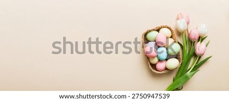 Happy Easter composition. Easter eggs in basket on colored table with yellow Tulips. Natural dyed colorful eggs background top view with copy space.