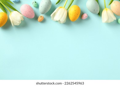 Happy Easter concept. Frame top border made of tulips spring flowers and colorful Easter eggs on light blue background.