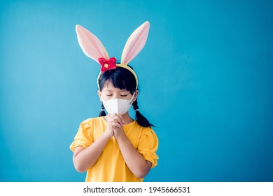 Happy Easter Day.Asian Child Girl Mask In Rabbit Ears Pray.Faith Prayer Online Worship In Easter Day Home.Kid Child Medical Mask.Healthcare, Easter Worship Home Church.Lockdown, Covid19 Coronavirus.