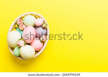Happy Easter. Easter eggs in basket on colored table with yellow roses. Natural dyed colorful eggs background top view with copy space.