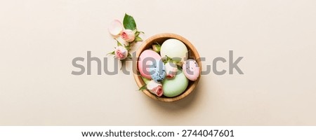 Happy Easter. Easter eggs in basket on colored table with yellow roses. Natural dyed colorful eggs background top view with copy space.