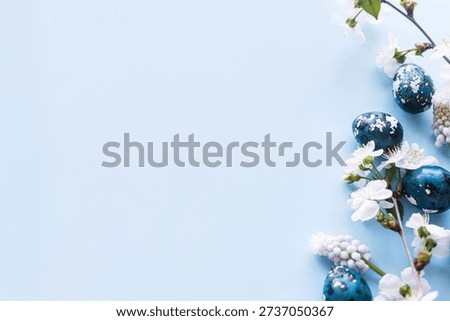 Happy Easter! Easter eggs with cherry blossom flat lay on blue background. Stylish spring template with space for text. Easter greeting card or banner