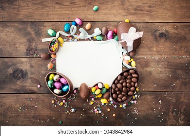 Happy Easter frame with greeting card with space for text,  chocolate eggs,  ribbon bows and candies on wooden background