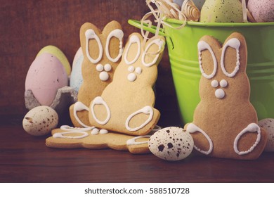Happy Easter gingerbread cookie bunnies with bucket of speckled Easter eggs on dark wood grain background, with applied retro style filters.
