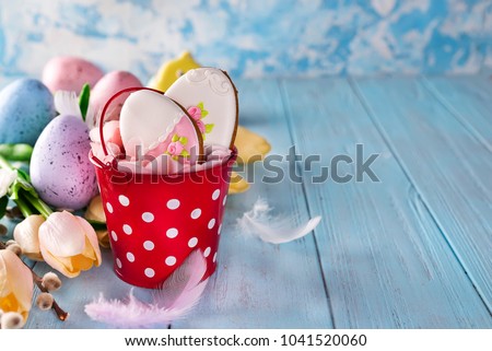 Happy Easter gingerbread cookie eggs with bucket and tulips with colorful eggs on blue wood background,
