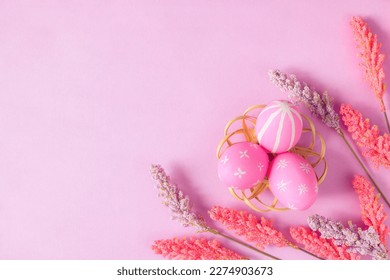 Happy Easter holiday greeting card concept. Colorful Easter Eggs and spring flowers on pastel pink background. Top view, flat lay, copy space.