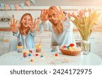 Happy Easter! Mom and daughter are having fun showing their hands on the camera stained with colorful Easter sweets, while they paint eggs preparing for the holiday.