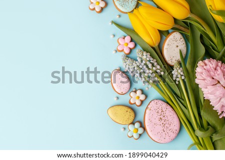 Happy Easter. Multi-colored pastel easter cookies gingerbread, seasonal flowers tulips on blue background. Easter concept, copy space, flyer, banner, coupon, greeting card, invitation